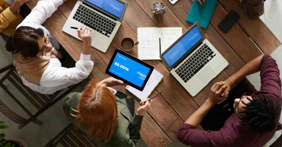 A team of professionals discussing escrow and risk management strategies over laptops during a technology contract meeting.