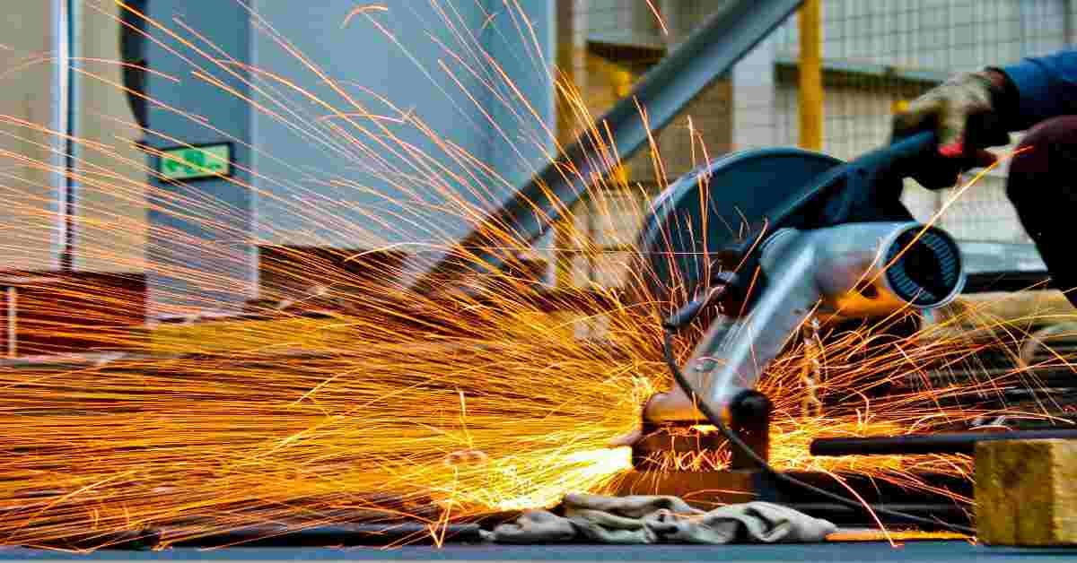 A worker using industrial metal cutting equipment in a factory, producing bright sparks during a precision metal stamping process.